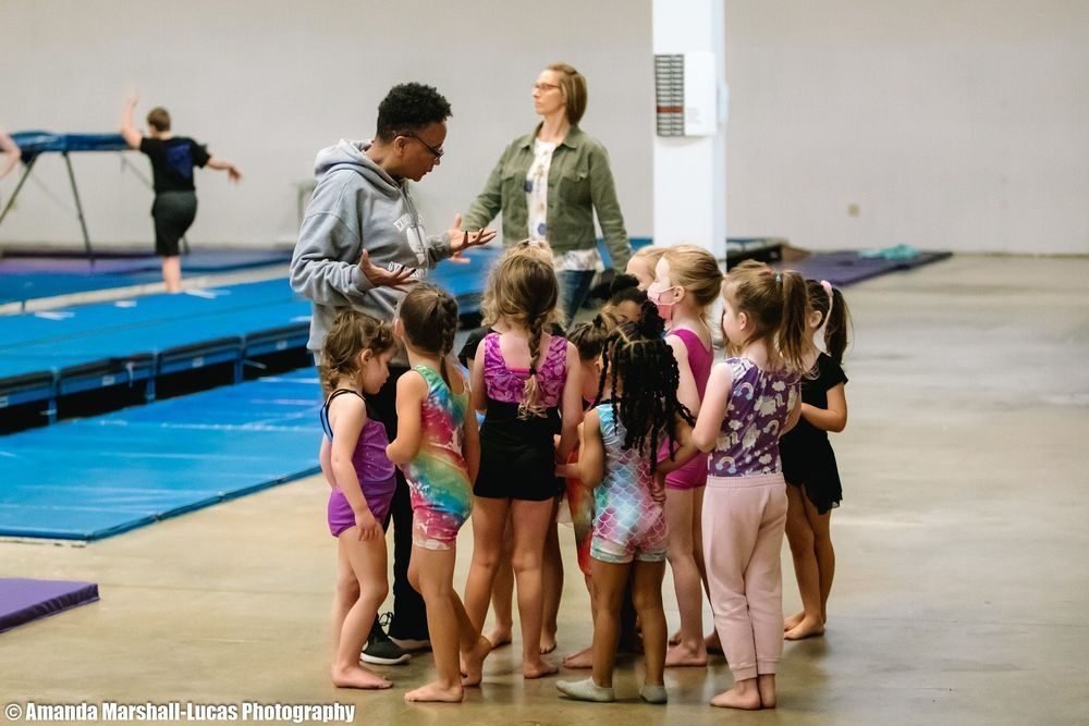 A group of young gymnasts with their coach on the floor